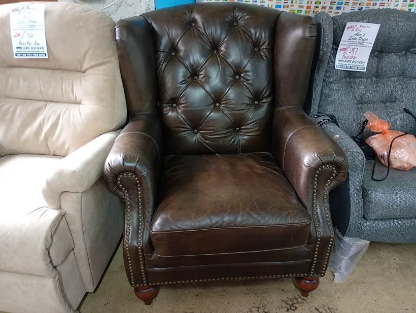Brown leather wing back armchair with buttoned tufted back, studded arms and turned wooden legs