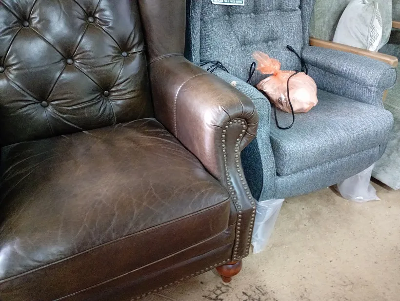 Brown leather wing back armchair with deep buttoned back and studded arms on wooden turned legs